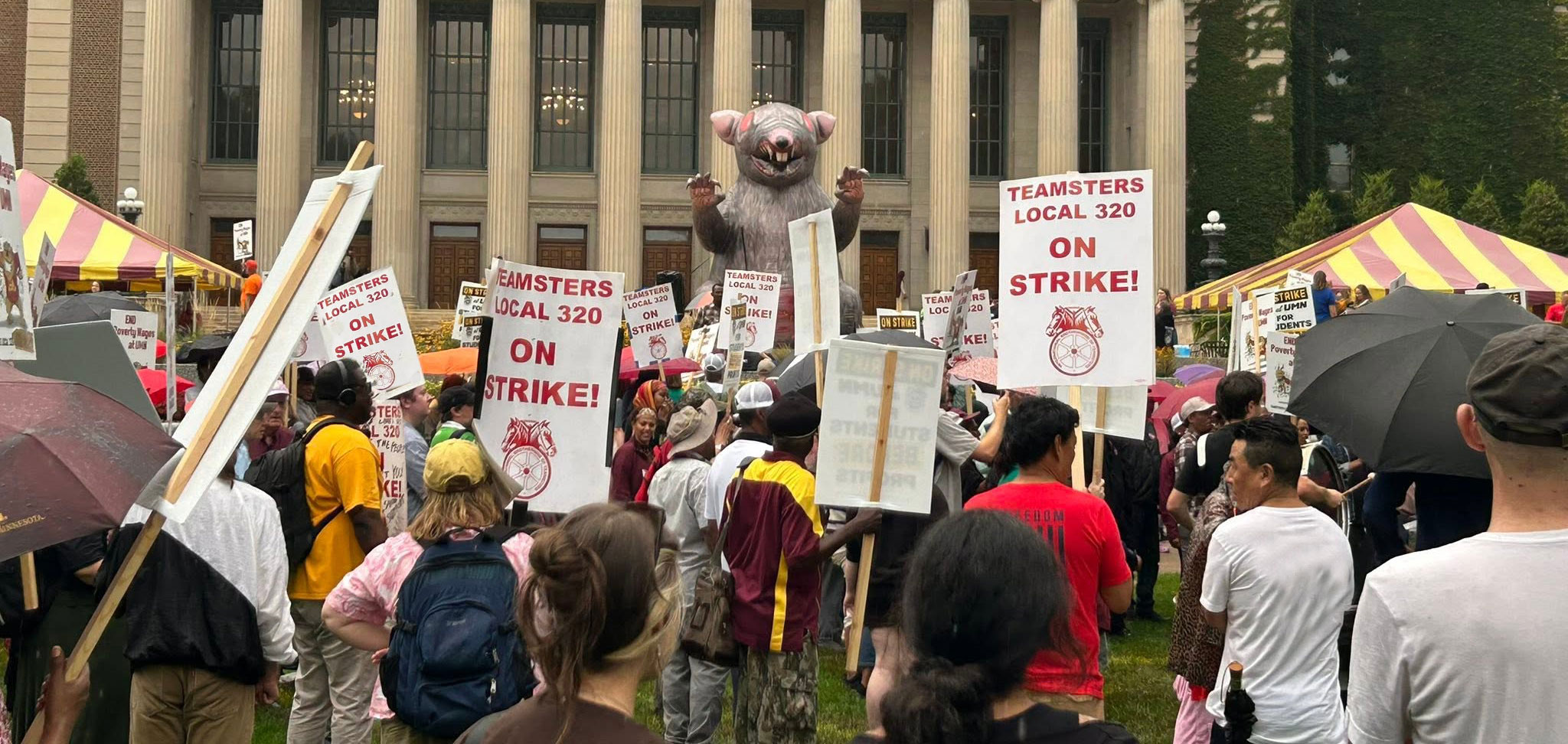 a group of striking workers with a giant inflatable rat